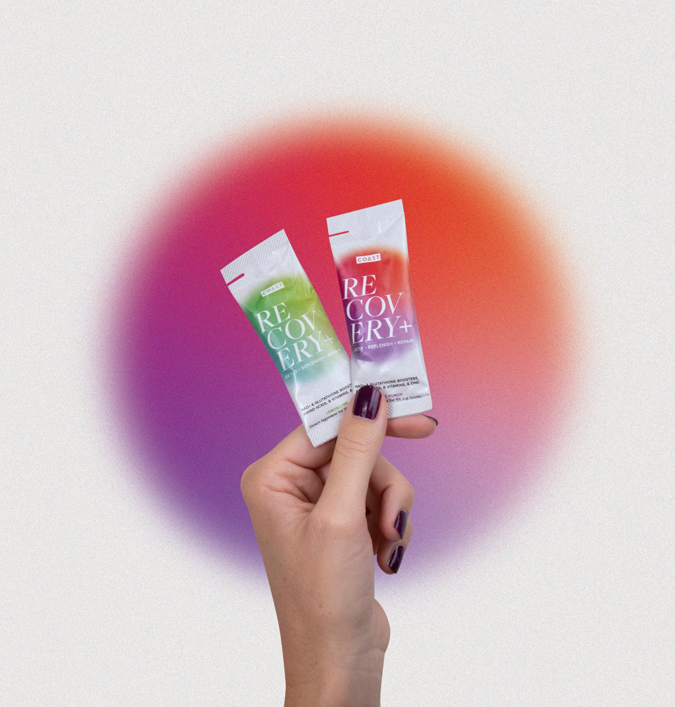 Hand holding two COAST Recovery+ powder sticks. Drink COAST Recovery+ daily to recover better by flushing out toxins, replenishing lost nutrients, and repairing cells. NAD+ and glutathione.